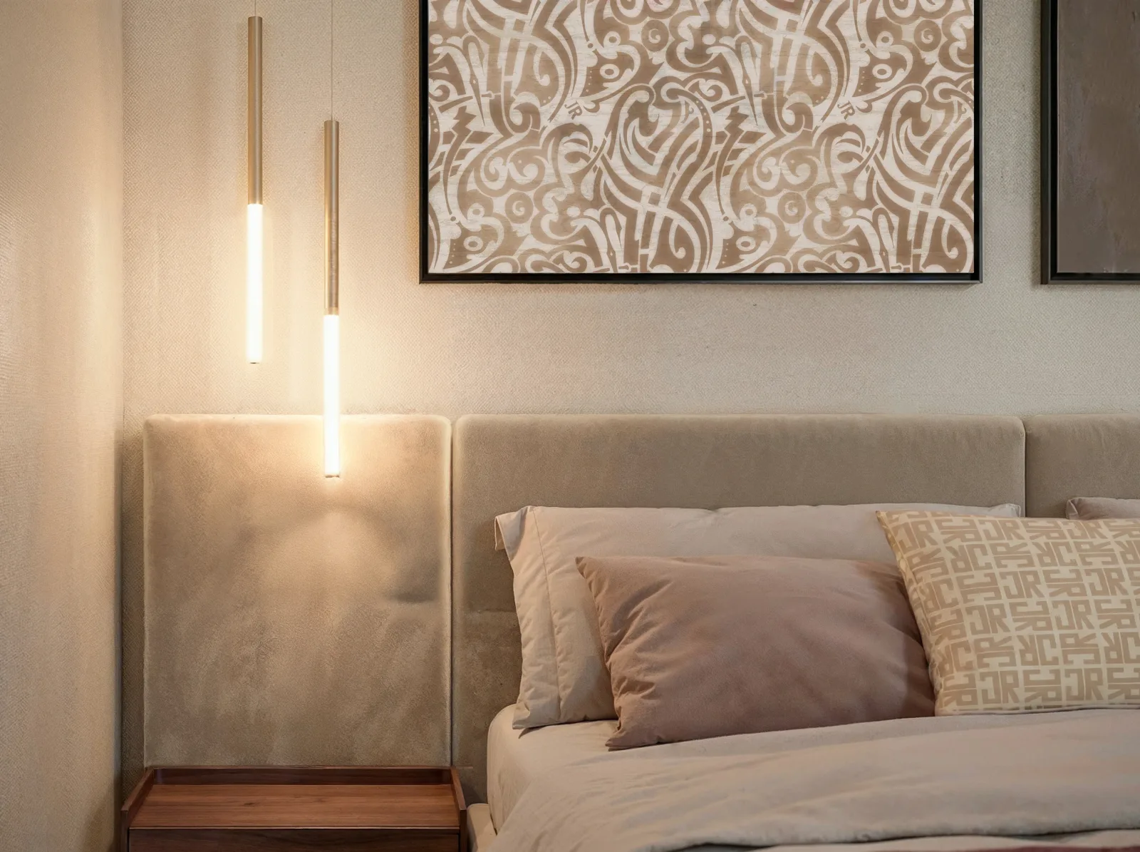 A close view of a bedhead: brass pendants over a suede panel, a monogrammed print above and the same monogram woven into the cushion