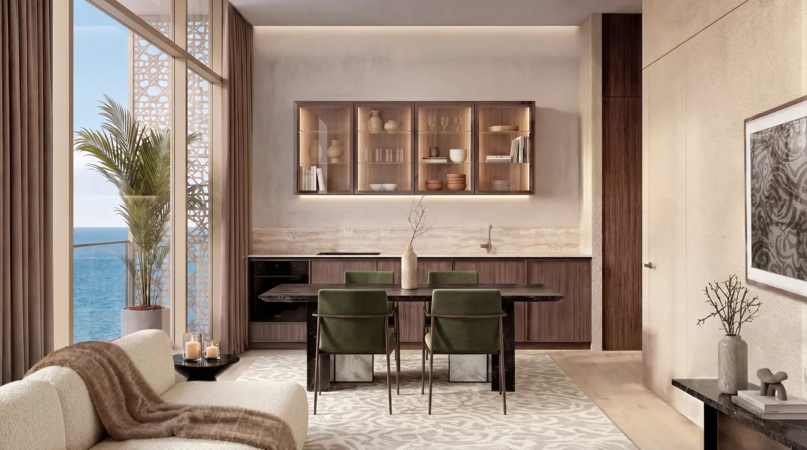 A walnut kitchen with lit glass-fronted cabinets, crockery and glassware on the shelves, a dining table and green velvet chairs in front of it
